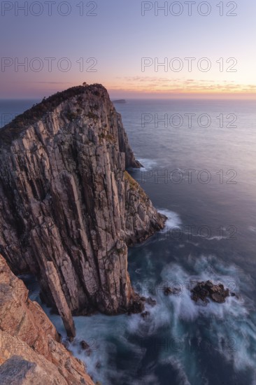 Totem Pole and The Lanterns. Long exposure at sunrise shows glowing dawn over the dramatic cliffs of Cape Hauy. Waves hit the steep cliffs. Cape Hauy, Tasman Peninsula, Tasmania, Australia