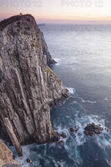 The Lanterns and Totem Pole Long exposure at sunrise shows glowing dawn over the dramatic cliffs of Cape Hauy. Waves hit the steep cliffs. Cape Hauy, Tasman Peninsula, Tasmania, Australia