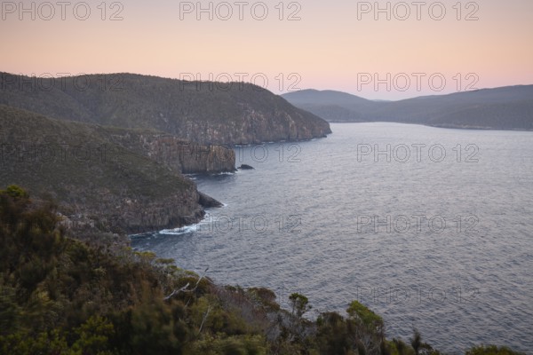 The Monument. Long exposure at sunrise shows glowing dawn over the dramatic cliffs of Cape Hauy. Gentle waves hit the steep cliffs. Cape Hauy, Tasman Peninsula, Tasmania, Australia