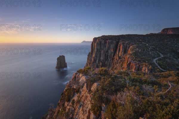 Long exposure at sunrise shows glowing dawn over the dramatic cliffs of Cape Hauy. View towards Cape Pillar. Hiking trail along the steep cliffs to Cape Hauy, Tasman Peninsula, Tasmania, Australia