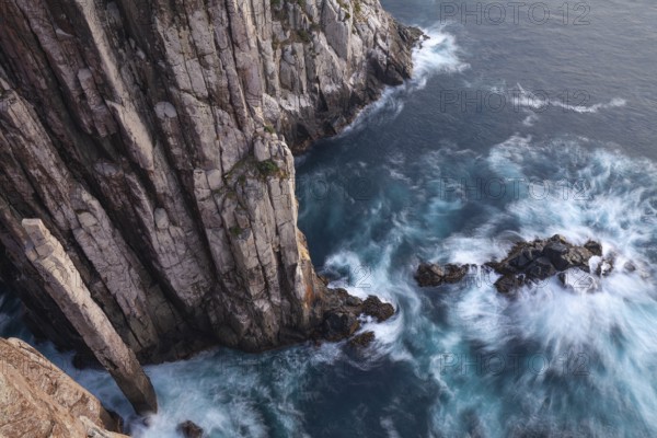Long exposure at sunrise shows glowing dawn over the dramatic cliffs of Cape Hauy. Gentle waves hit the steep cliffs. Cape Hauy, Tasman Peninsula, Tasmania, Australia