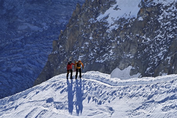 Two ascended mountaineers run across a snow-covered mountain ridge, Aiguille du Midi, Chamonix-Mont-Blanc, Haute-Savoie, France