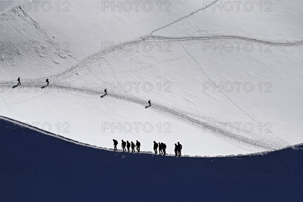 A group of mountaineers runs across a snow-covered mountain ridge, Aiguille du Midi, Chamonix-Mont-Blanc, Haute-Savoie, France