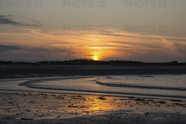 Sunset on a quiet beach with soft light on the waves, wet beach at low tide, dunes in the background, atmospheric, glowing, calm, warm atmosphere, reflecting light on water and beach, reflection, warm and cool tones, orange, yellow, gold, blue, grey, clouds, evening, shade, sandy beach, sand, shore, nobody, maritime, deserted sea, soft waves, surf, swell, sea, swell, swell, sea, Aade Bay, North Sea, Dune Island, Heligoland, Pinneberg District, Schleswig-Holstein, Germany
