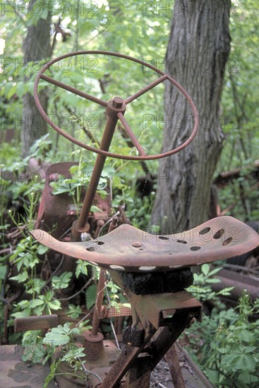 Rusted wheel and iron seat from an American tractor around 1900, deposited in a wooded area, Marksboro, New Jersey, USA