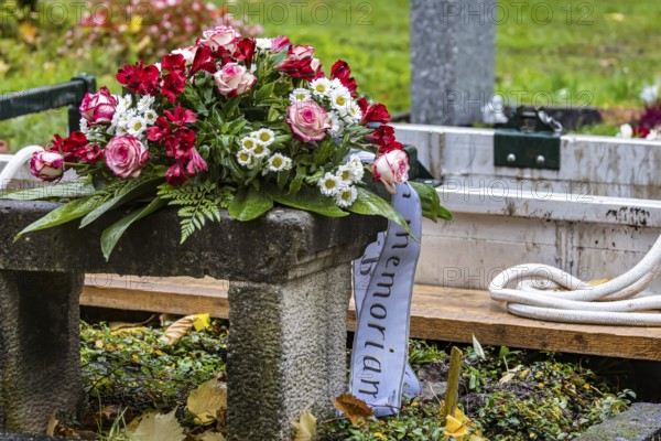 Open grave with a funeral wreath just in front of the burial of a deceased person. Pragfriedhof Stuttgart in autumn. Stuttgart, Baden-Württemberg, Germany