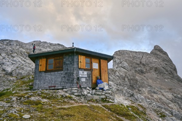Two mountaineers relax at the Wildalmkirchl bivouac with the Wildalmkirchl summit in the background, Steinernes Meer, Berchtesgaden Alps, Austria