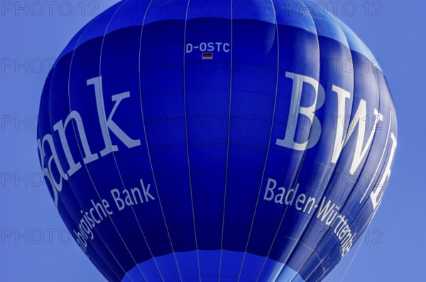 A hot air balloon, registration D-OSTC, rises into the air as part of an air show at the Rossfeld Air Sports Association's Flying Festival on Rossfeld in Metzingen-Glems, Baden-Württemberg, Germany, for editorial use only