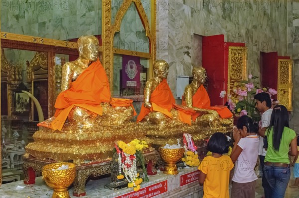 Buddhist believers Buddhists pray making offerings to statues of Buddhist monks covered with gold leaf at Wat Chalong Monastery, Wat Chaithararam, Phuket Island, Phuket Province, Thailand