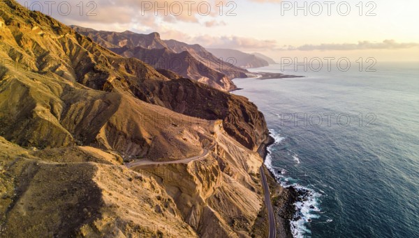 Desert landscape converges with ocean along a rugged coastal area, shore break at cliffs, blue cloudy sky at sunset, dry landscape in an aerial drone view, AI generated