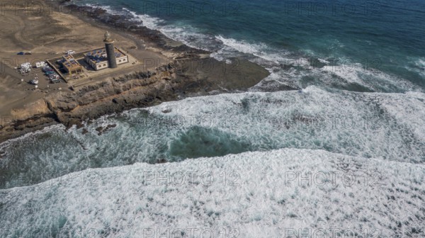 Aerial view of Faro Punta de Jandia lighthouse at the southern tip of Jandia peninsula, in the foreground white foam crowns on moving sea swell large high waves on reef edge beaming sea strong surf, Fuerteventura, Canary Islands, Canary Islands, Spain