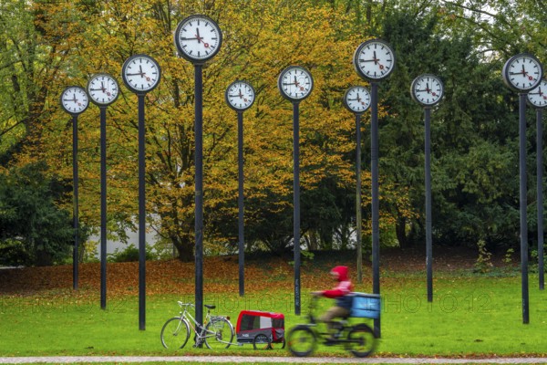 The art installation Zeitfeld in Volksgarten Park in Düsseldorf-Oberbilk, a total of 24 station clocks, on 6 meter high steel columns, have been running synchronously since 1987, cyclists in the municipal park, artwork by Düsseldorf artist Klaus Rinke, symbol of time, time change, North Rhine-Westphalia, Germany