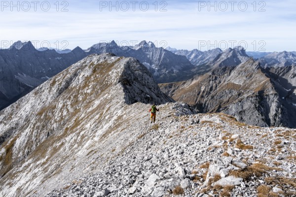 Hikers on the summit ridge of the Gamsjoch, behind rock faces of the Laliderer Spitze, eastern Karwendel, Tyrol, Austria