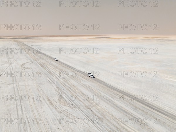 Aerial view, two off-road cars driving on a salt pan, arid landscape, Botswana
