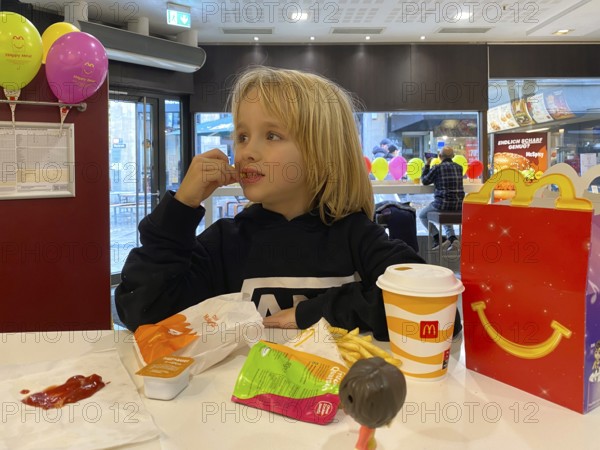 Interior view, child, boy, 7 years, blonde, eating Happy Meal, children's menu, at McDonald's restaurant, drink, French fries, ketchup, balloons, logo, Stuttgart, Baden-Württemberg, Germany