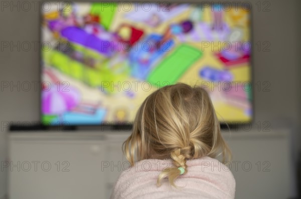 Child, girl, 4 years old, blonde, lying on sofa, watching TV, watching television, in front of television, from behind, braid, monitor, children's program, children's program, children's television, colorful, Stuttgart, Baden-Württemberg, Germany