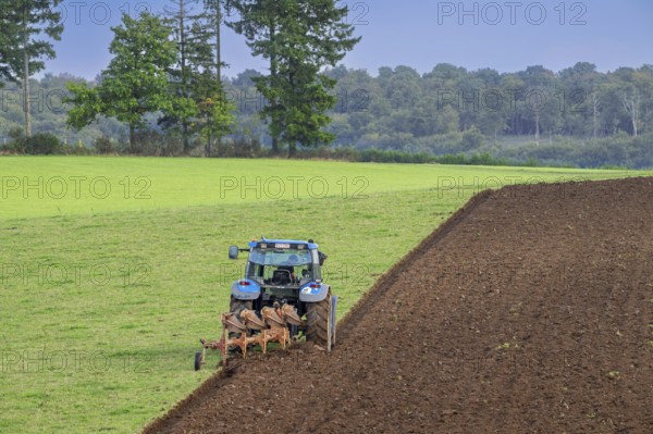 Tractor with plough, agricultural ploughing machine working on a field in autumn, fall in the Belgian Ardennes, Luxembourg, Wallonia, Belgium