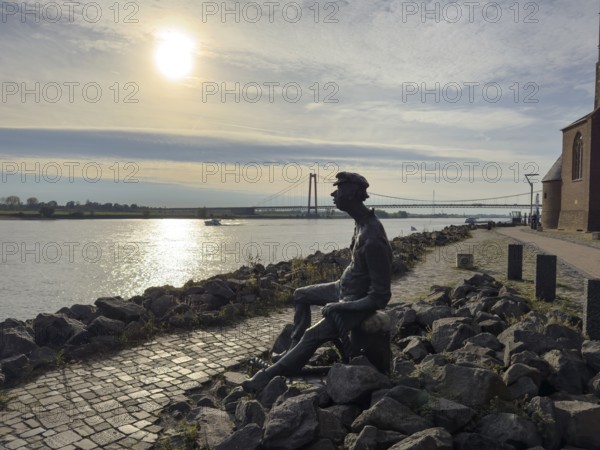 Photo with melancholy mood of bronze sculpture Poortekerl looking at Rhine waiting for ship to unload, Rhine navigation inland shipping, reminiscence of old times, bronze statue by artist Heide Friede-Kinalzik, Emmerich, Lower Rhine, North Rhine-Westphalia, Germany