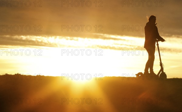E-scooter drivers ride across a dike on the island of Fehmarn at sunset, 13.10.2025, Fehmarn, Schleswig-Holstein, Germany