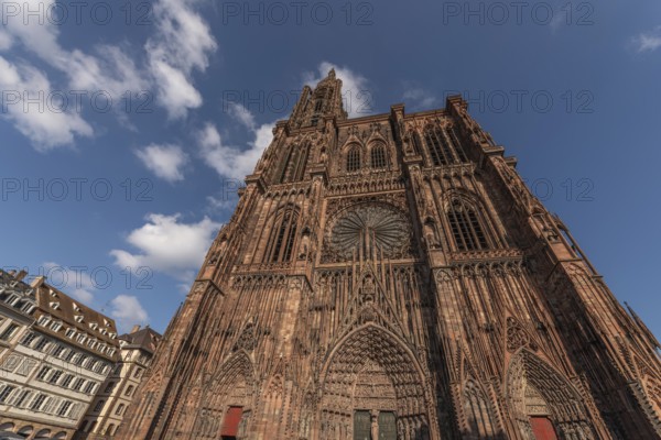 Strasbourg's Notre Dame Cathedral stands majestically there. Its magnificent architectural details are clearly visible under the blue, cloudy sky. Bas Rhin, Alsace, France