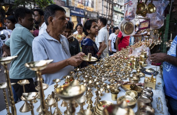 People shop for bronze and other metal items at a roadside stall on Dhanteras, in Guwahati, Assam, India on 18 October 2025. On Dhanteras, people traditionally buy precious metals like gold, silver, or even new utensils, as it is believed this brings wealth and good luck into the household
