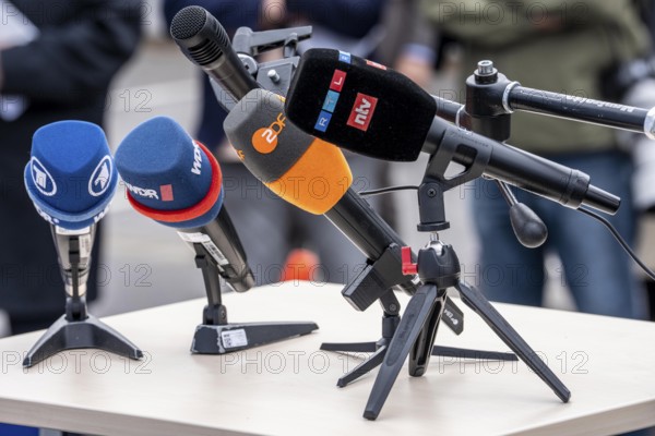 Microphones from various radio stations, television stations, standing on the table, at a press conference