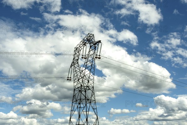 High voltage power lines against a bright blue sky with scattered clouds, Puy de Dome, Auvergne Rhone Alpes, France
