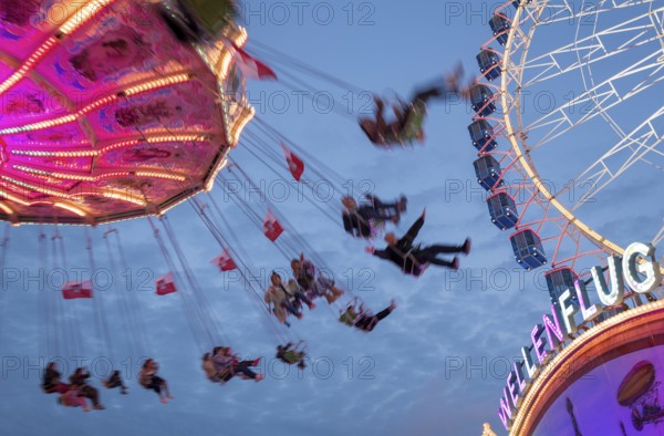 An illuminated chain carousel turns at night at a funfair, with floating people and colourful lights, Bad Cannstatt, Stuttgart, Baden-Württemberg, Germany