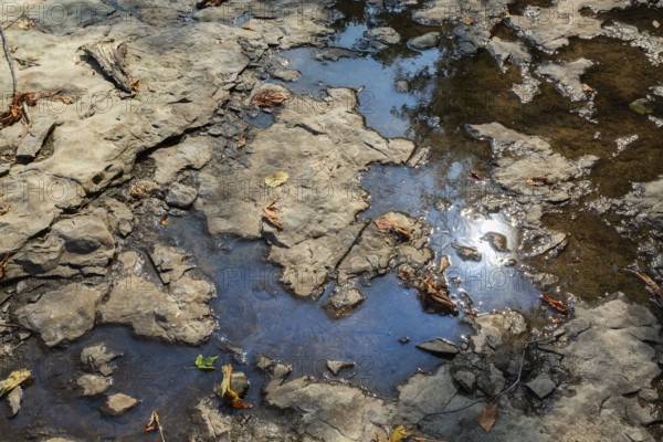 Accidental spilled oil in puddle of water in dried out flat rock river bed due to lack of rainfall during hot and dry summer, Laval, Quebec, Canada