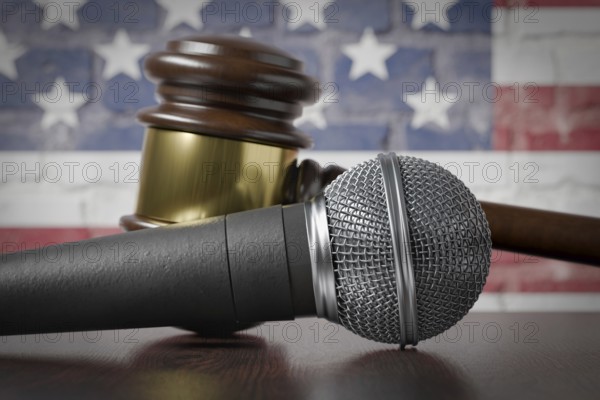 Microphone and gavel resting on a table with the american flag painted on A brick wall behind