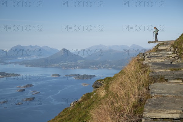 Woman with walking sticks standing on a ledge, Rørsethornet stone stairs, with 3292 steps one of the longest continuous stone stairs in the world, Sherpat stairs or Midsund stairs or Midsundtrappene, Rørsethornet hike, Otroya or Otrøya island, Møre og Romsdal, Norway