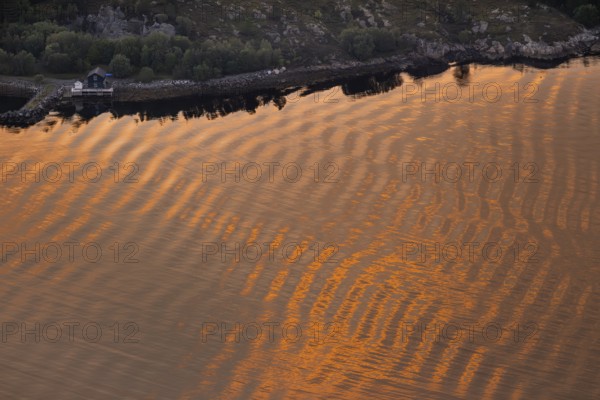 Warm sunlight reflects on gentle waves in a bay at sunset, forming a wave-like pattern, Otroya or Otrøya Island, Møre og Romsdal, Norway