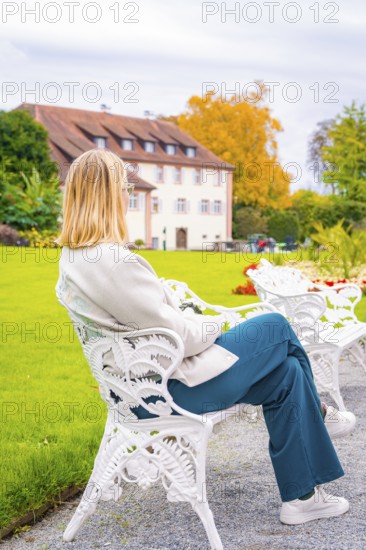 Rear view of a woman on a white bench in the garden, Mainau flower island, Lake Constance, Germany