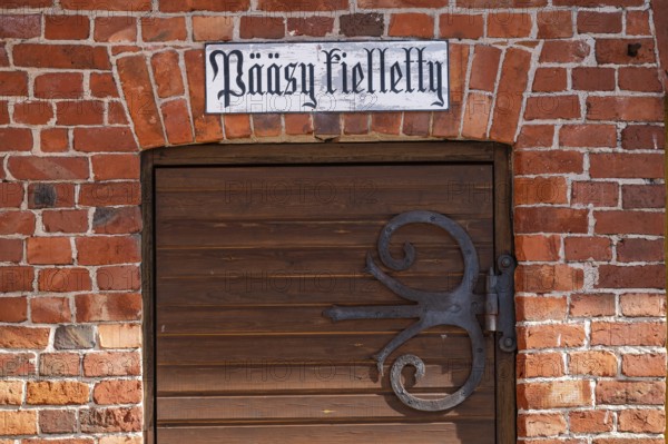 Wrought-iron fitting on wooden door and sign with Finnish inscription 'pääsy kielletty', no entry, brick wall, former paper mill for the production of groundwood pulp board, UNESCO World Heritage Site Verla Factory Village, Maailmanperintökohde Verlan puuhiomo ja pahvitehdas, Verla Rapids, Kymenlaakso, near Kouvola, Finland
