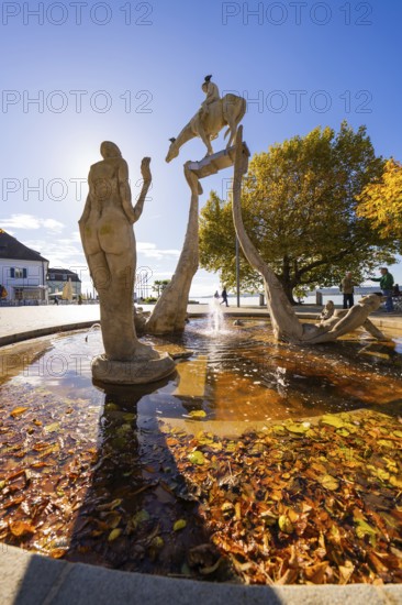 Artistic fountain with sculptures surrounded by autumn leaves and water, Überlingen, Lake Constance, Germany