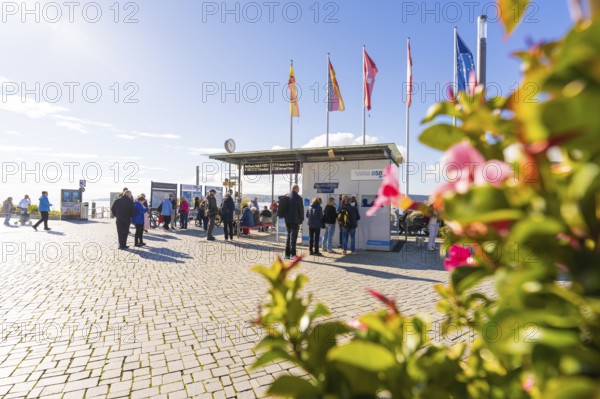 Crowd in front of a harbour building with flags and sunny cobblestones, Überlingen, Lake Constance, Germany