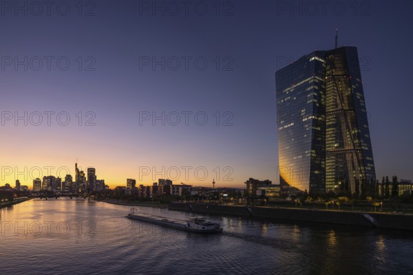 A boat cruises along the Main at sunset, in front of the European Central Bank (ECB) and the Frankfurt banking skyline, Frankfurt am Main, Hesse, Germany