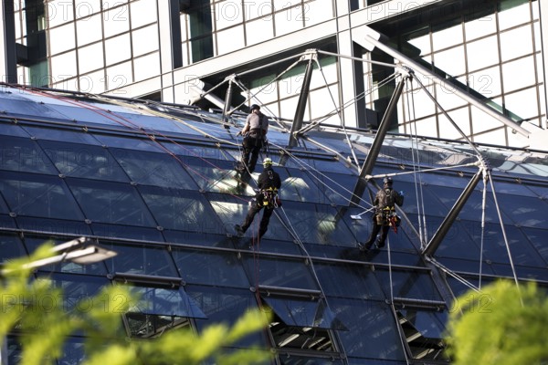Three male glass cleaners abseiling down a glass roof of Berlin Central Station to clean windows, Berlin, Germany