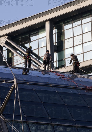 Three male glass cleaners abseiling down a glass roof of Berlin Central Station to clean windows, Berlin, Germany