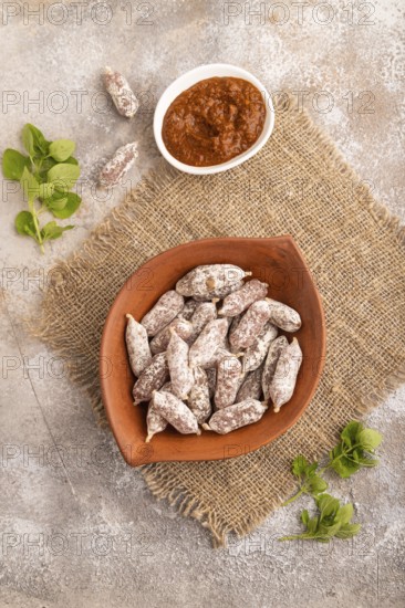 Small smoked Chicken sausages in clay bowl on brown concrete background and linen textile. top view, flat lay, close up