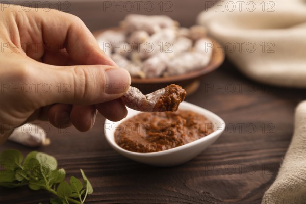 Small smoked Chicken sausages in wooden bowl with hand on brown wooden background and linen textile. side view, close up, selective focus