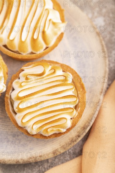 French lemon tart with meringue on brown concrete background, cup of coffee, orange linen textile, side view, close up, selective focus