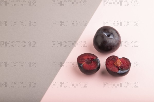 Purple Plum Cut in half on pink and gray pastel paper background. Side view, copy space. healthy food, vegetable, minimalism