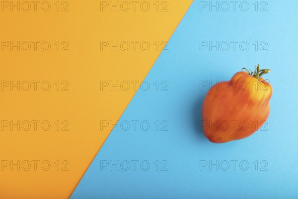 Red Heart Shape tomato on blue and orange pastel paper background. Top view, flat lay, copy space. healthy food, vegetable, minimalism