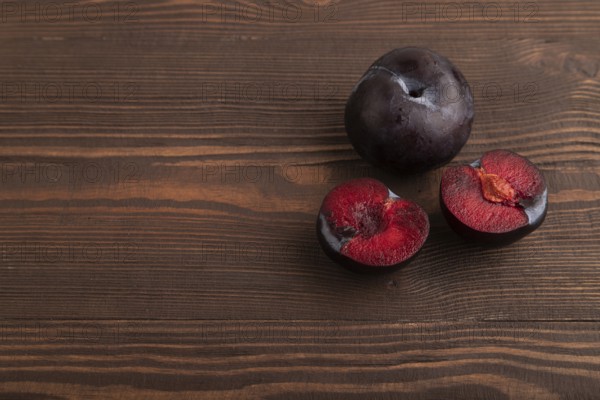 Purple Plum Cut in half on brown wooden background. Side view, copy space. healthy food, vegetable, minimalism