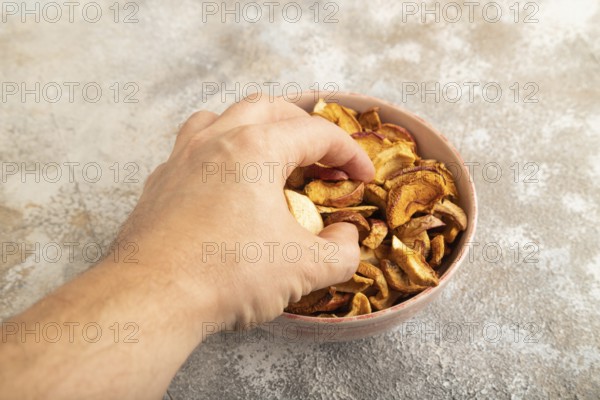 Dried Apples in ceramic bowl with hand on brown concrete background. Side view, copy space, flat lay. healthy food, minimalism. sweet