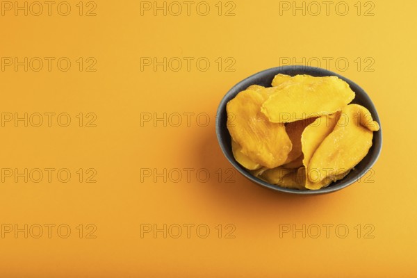 Dried Mango in blue ceramic bowl on orange pastel paper background. Side view, copy space. healthy food, minimalism