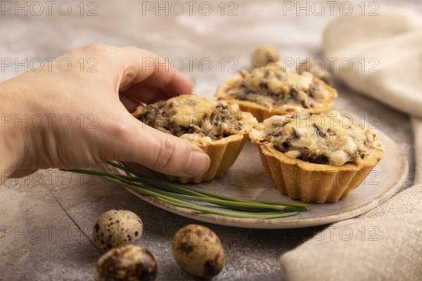 Tartlets with meat and cheese with hand on brown concrete background and linen textile. side view, close up, selective focus