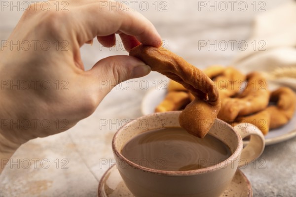 Crunchy biscuit Brushwood cookies with hand sprinkled with powdered sugar on brown concrete background and linen textile, cup of coffee, side view, selective focus