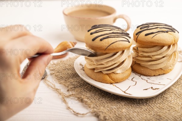 Caramel Cream Cakes with hand on white wooden background and linen textile, cup of coffee, side view, close up, selective focus